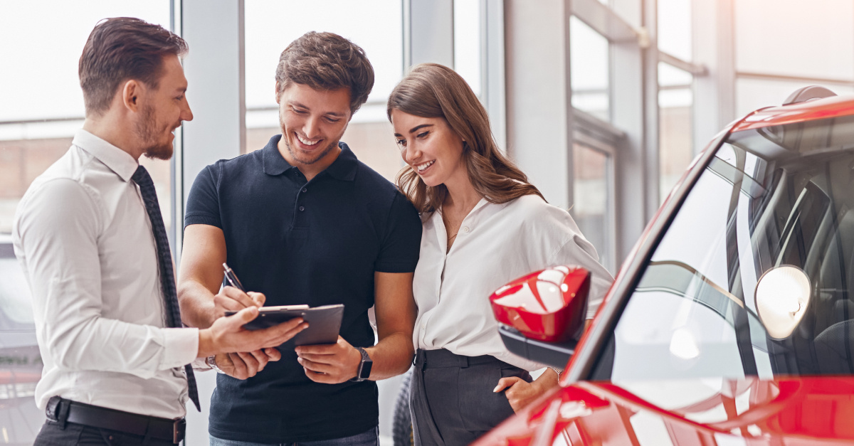 Delighted couple and manager signing papers in car dealership
