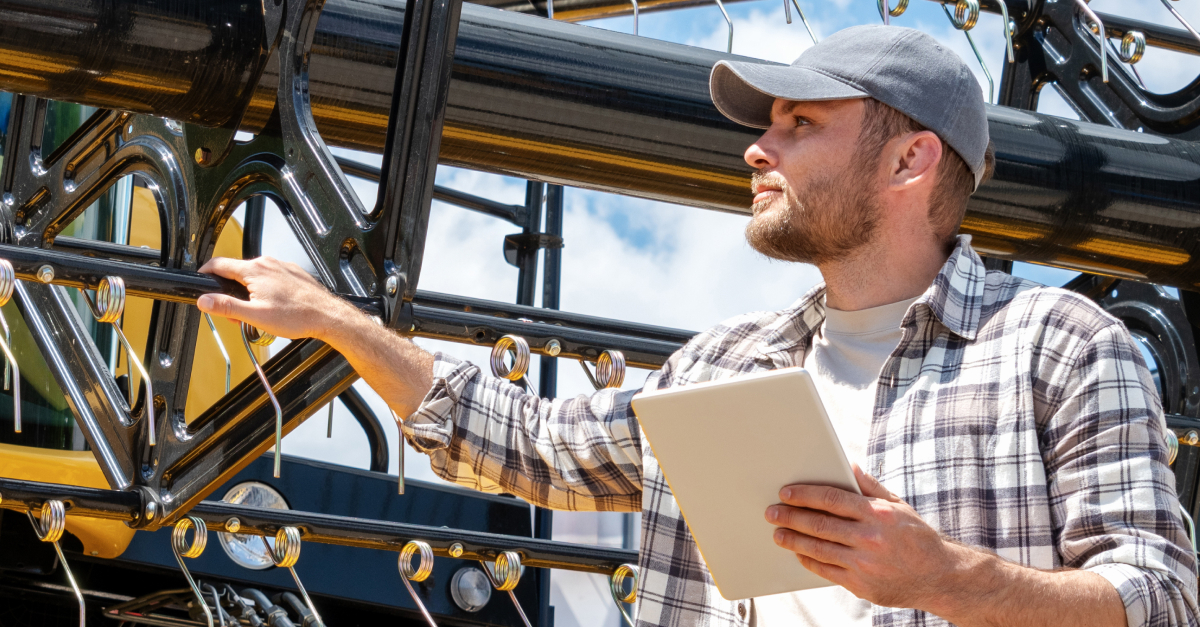 Caucasian man with digital tablet in hand looking at new yellow combine harvester at agricultural equipment dealership