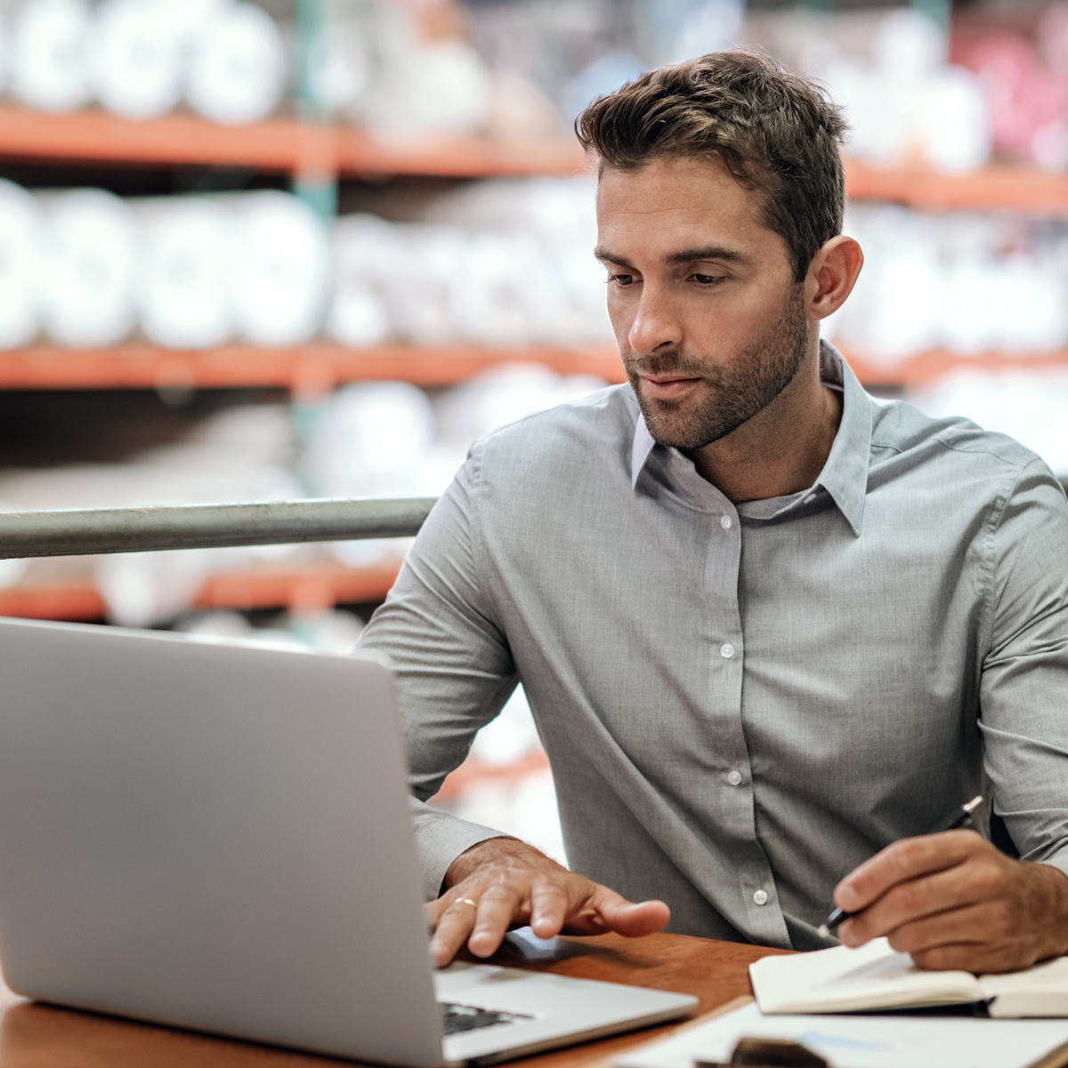 Warehouse manager taking notes and checking orders with a laptop