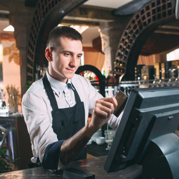 happy man or waiter in apron at counter with cashbox working at bar or coffee shop